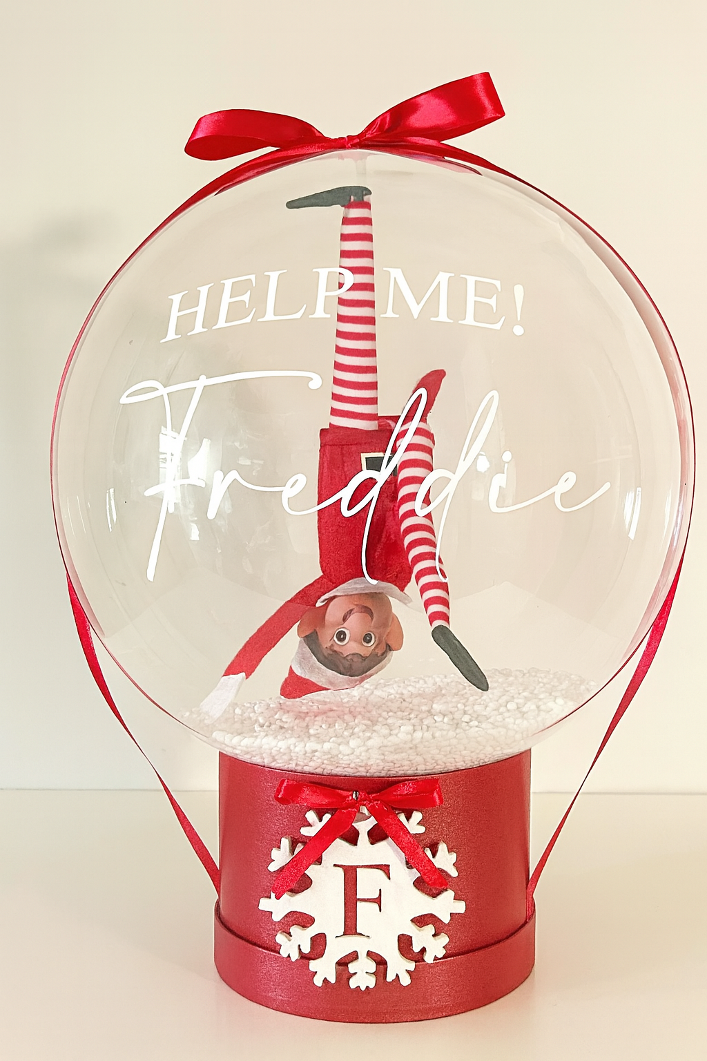 Clear snow globe balloon showing upside-down elf toy and festive message — personalized Christmas surprise